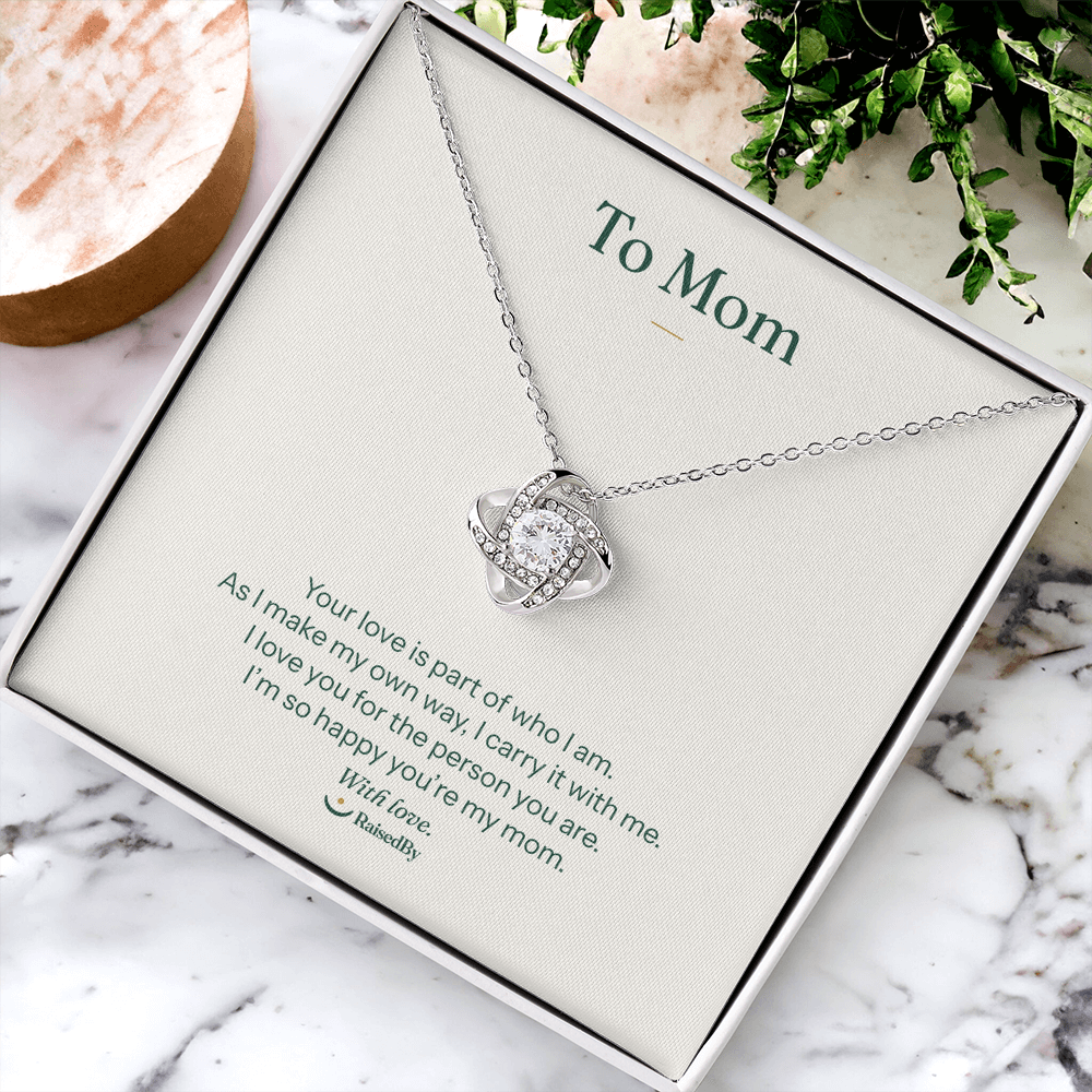 14K white gold finish Love Knot necklace and To Mom message card on marble beside flowers